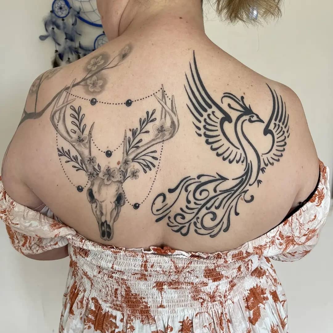 A detailed blackwork tattoo featuring a deer skull and phoenix design on the back.