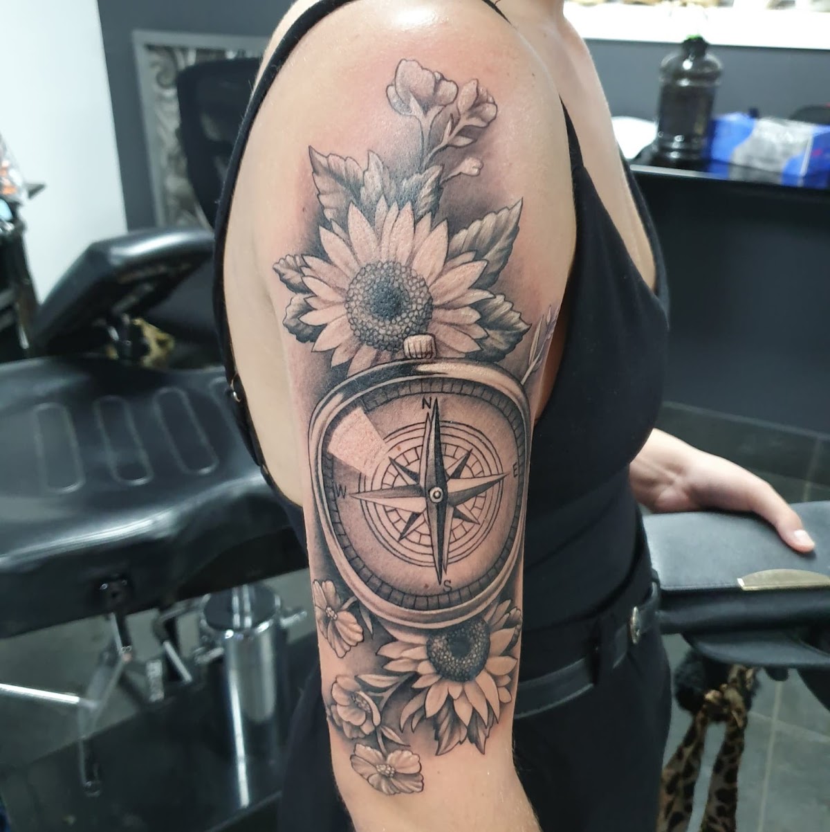 A detailed black and grey sunflower compass tattoo adorns the upper arm.