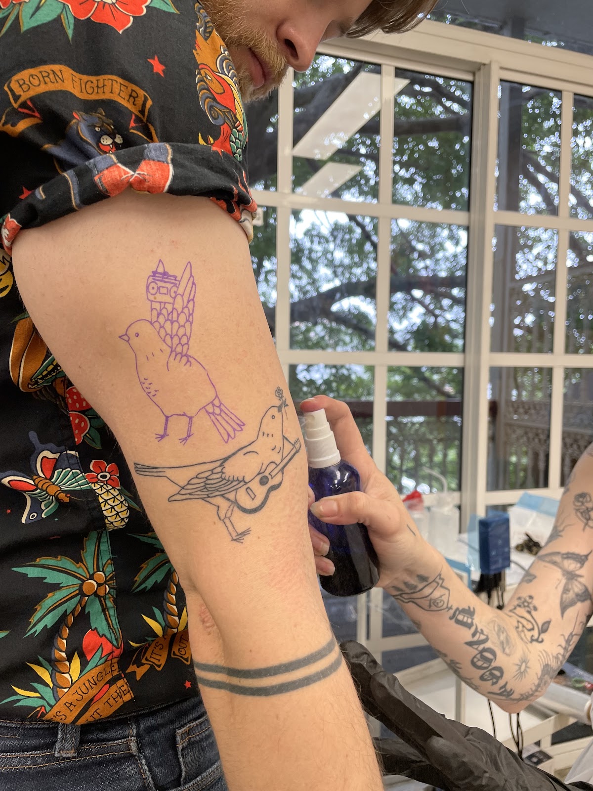 A linework bird tattoo with a musical instrument being sketched on the arm.