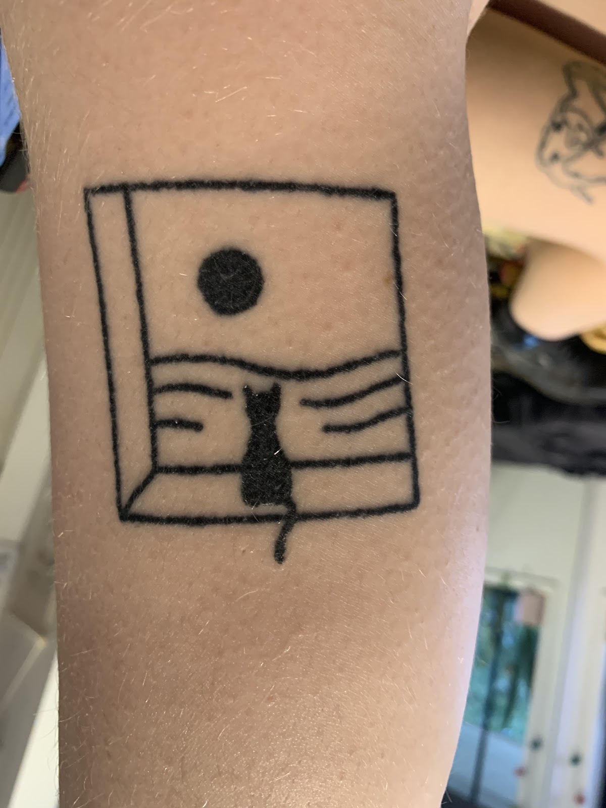 A linework tattoo of a book with a cat reading inside.