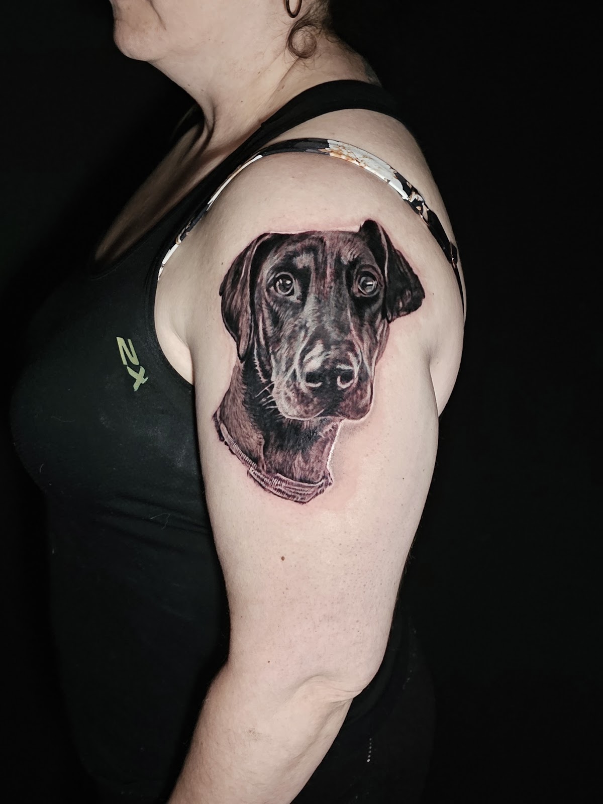 A detailed black and grey portrait of a dog tattoo on the upper arm.