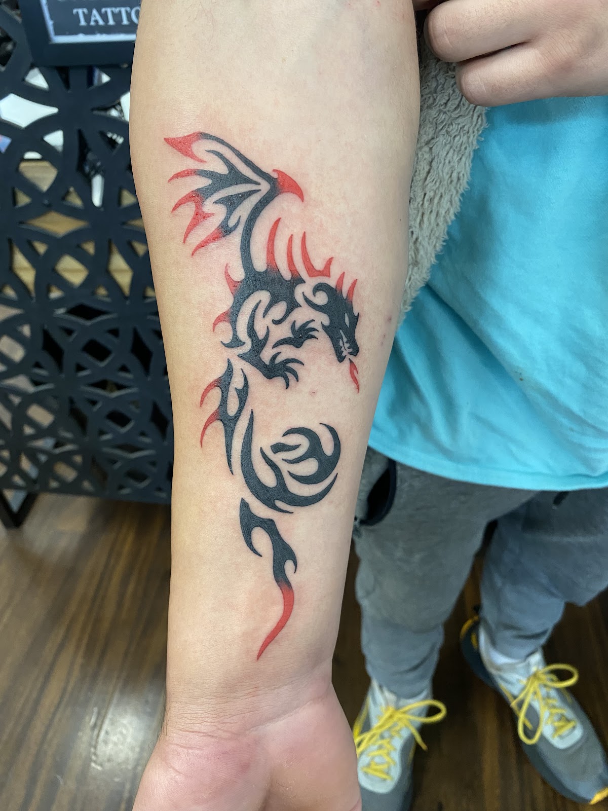 A vibrant dragon tattoo with fiery accents adorns the forearm.