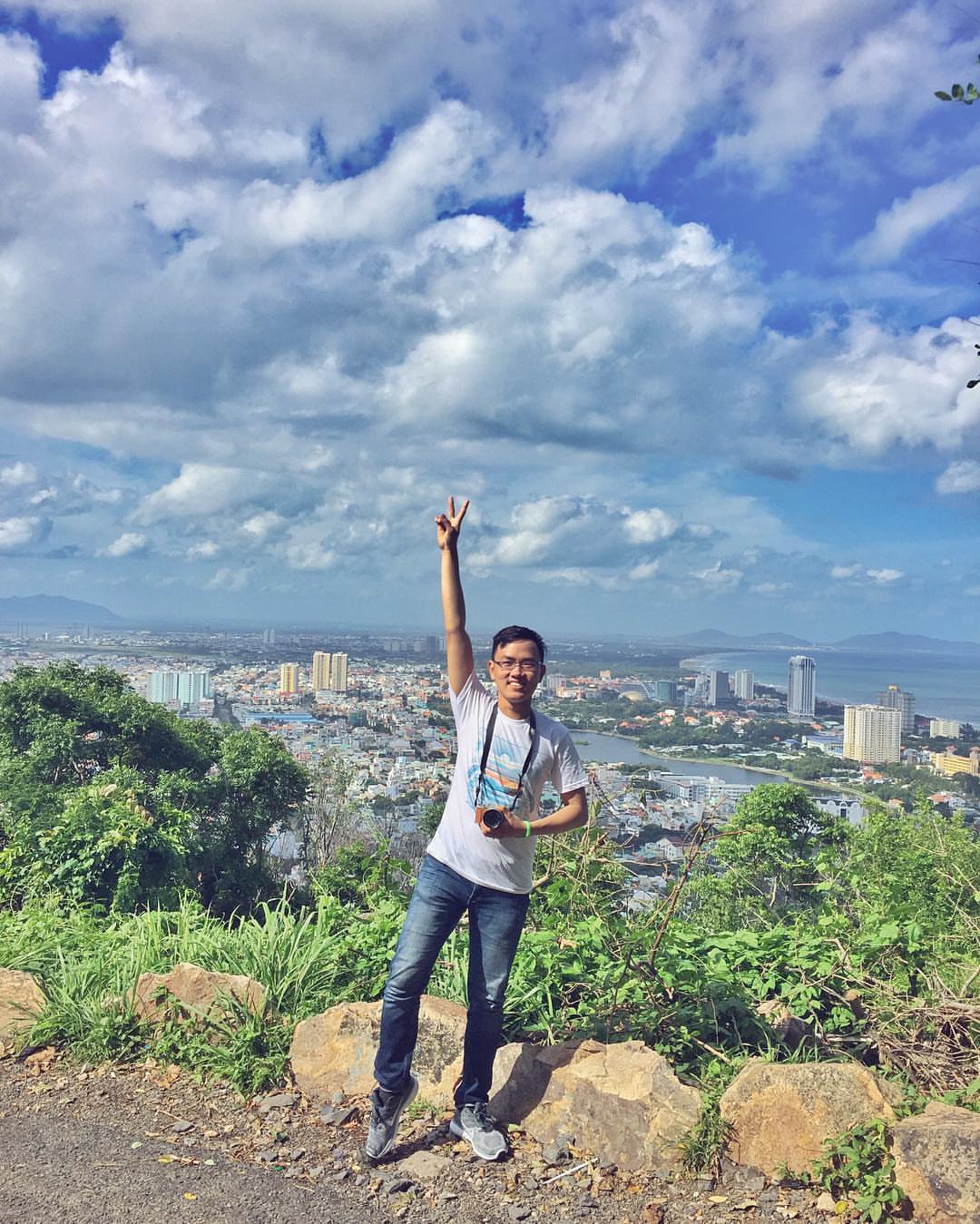 A traveler posing with his camera on the peak of a mountain