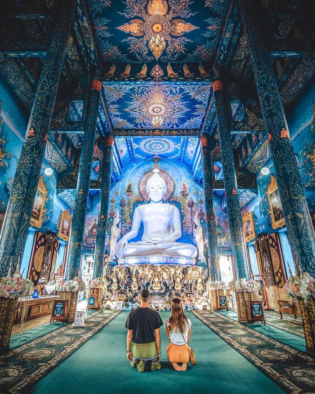 A couple praying in the main hall of a temple during their travel to Thailand