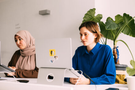 Twee vrouwen geven een webinar achter laptops over inclusie, de linkse vrouw is gesluierd.