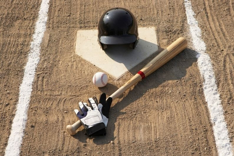 A baseball bat, helmet, and gloves lie on a base.