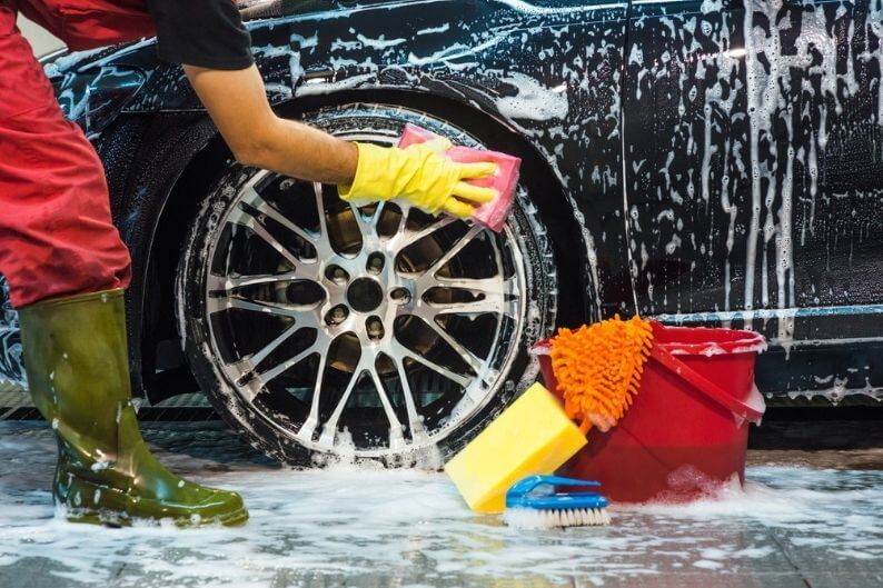 Man hand washes car wheel at a car wash franchise.