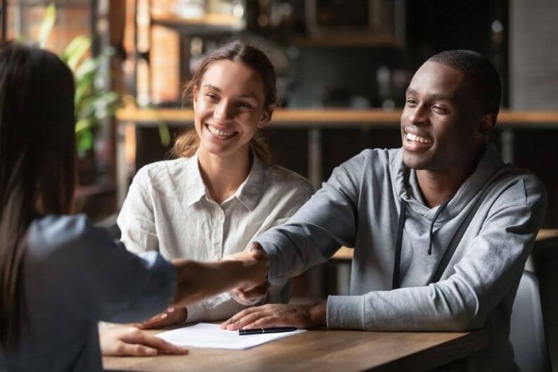 Couple shakes hands with bank representative after securing a loan for their franchise financing.