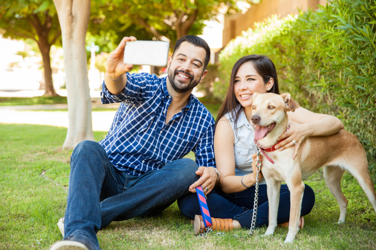 A man and woman pose for a selfie with their dog.