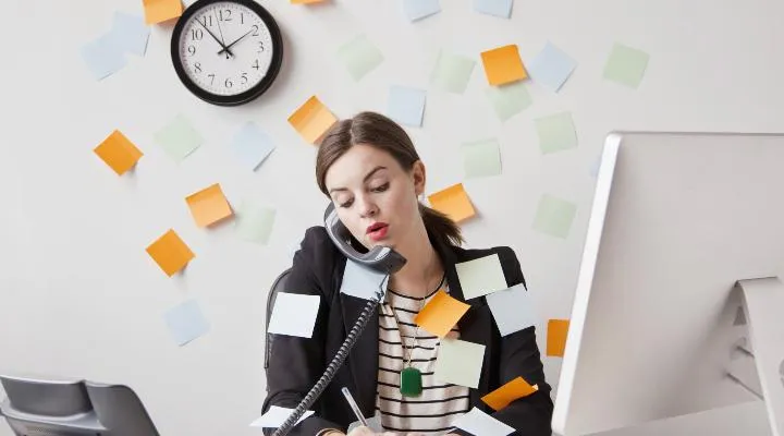 Donna impegnata al telefono con post-it e orologio.
