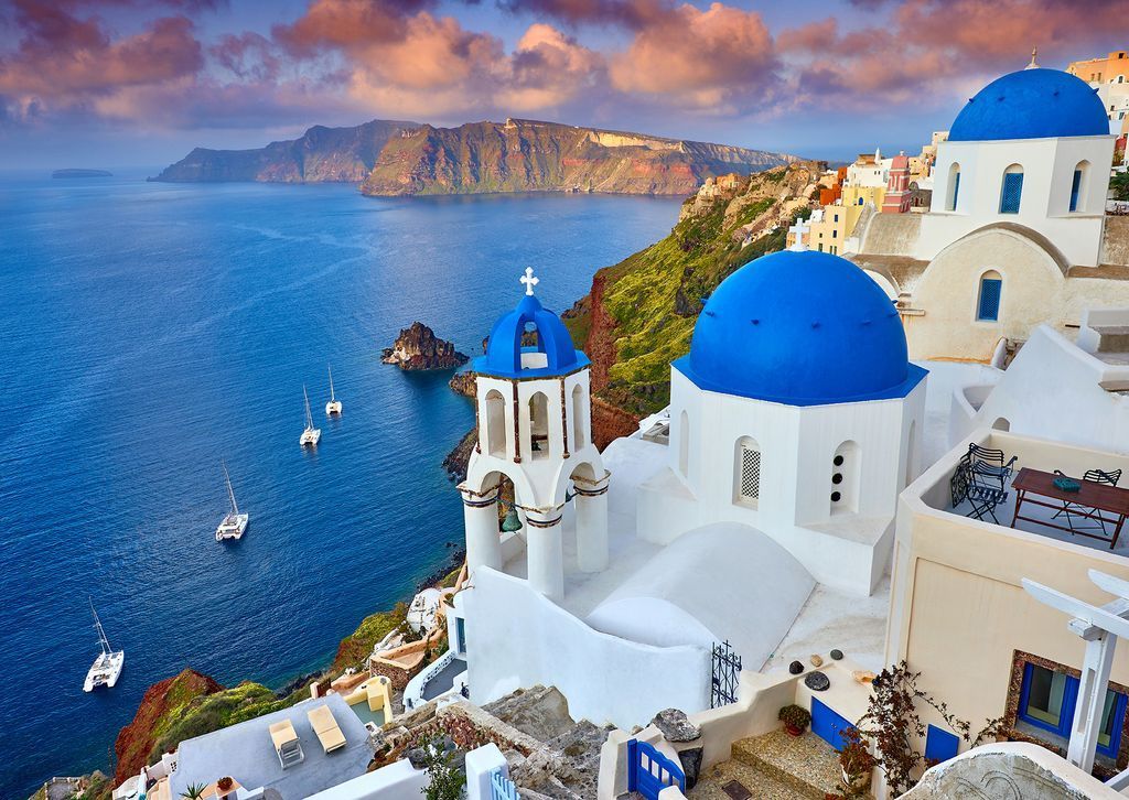 Iconic blue-domed Greek churches overlooking a deep blue caldera sea at sunset.