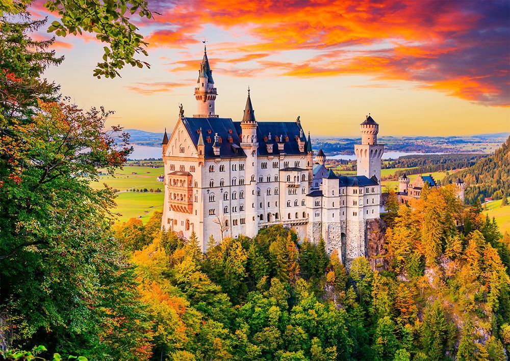 A fairytale castle nestled in a forest during autumn under a vibrant, fiery sunset.