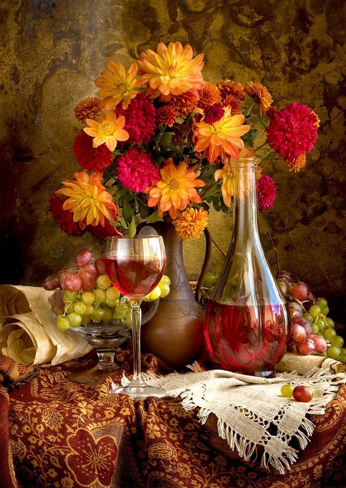 Still life with a bouquet of autumn-colored dahlias, a glass of wine, and grapes on a decorative patterned cloth.