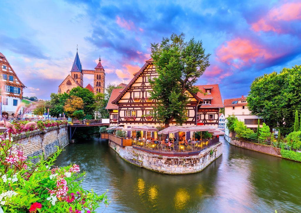 A riverside German half-timbered building at sunset with a cathedral in the background.