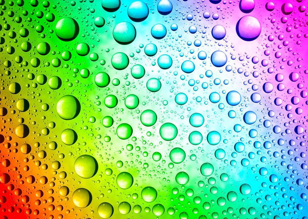 A vibrant spectrum of water droplets on a multicolored background, transitioning from red to purple.