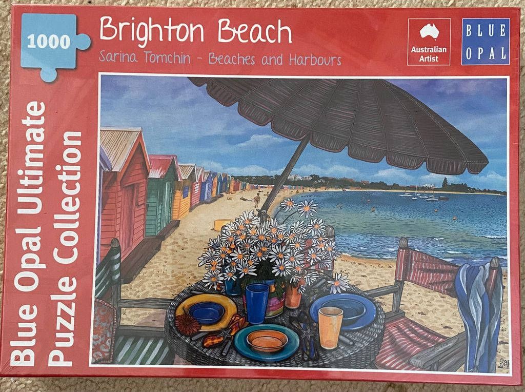 Painting of a beachside table set with daisies and tableware in front of colorful bathing boxes at Brighton Beach.