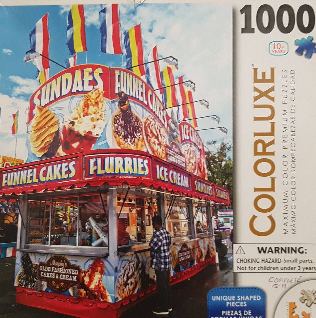 A carnival food stand advertising sundaes, funnel cakes, and ice cream under a row of colorful flags against a blue sky.