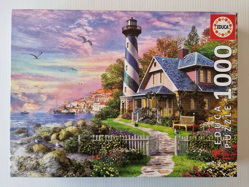 A lighthouse and cottage by a seaside town at sunset