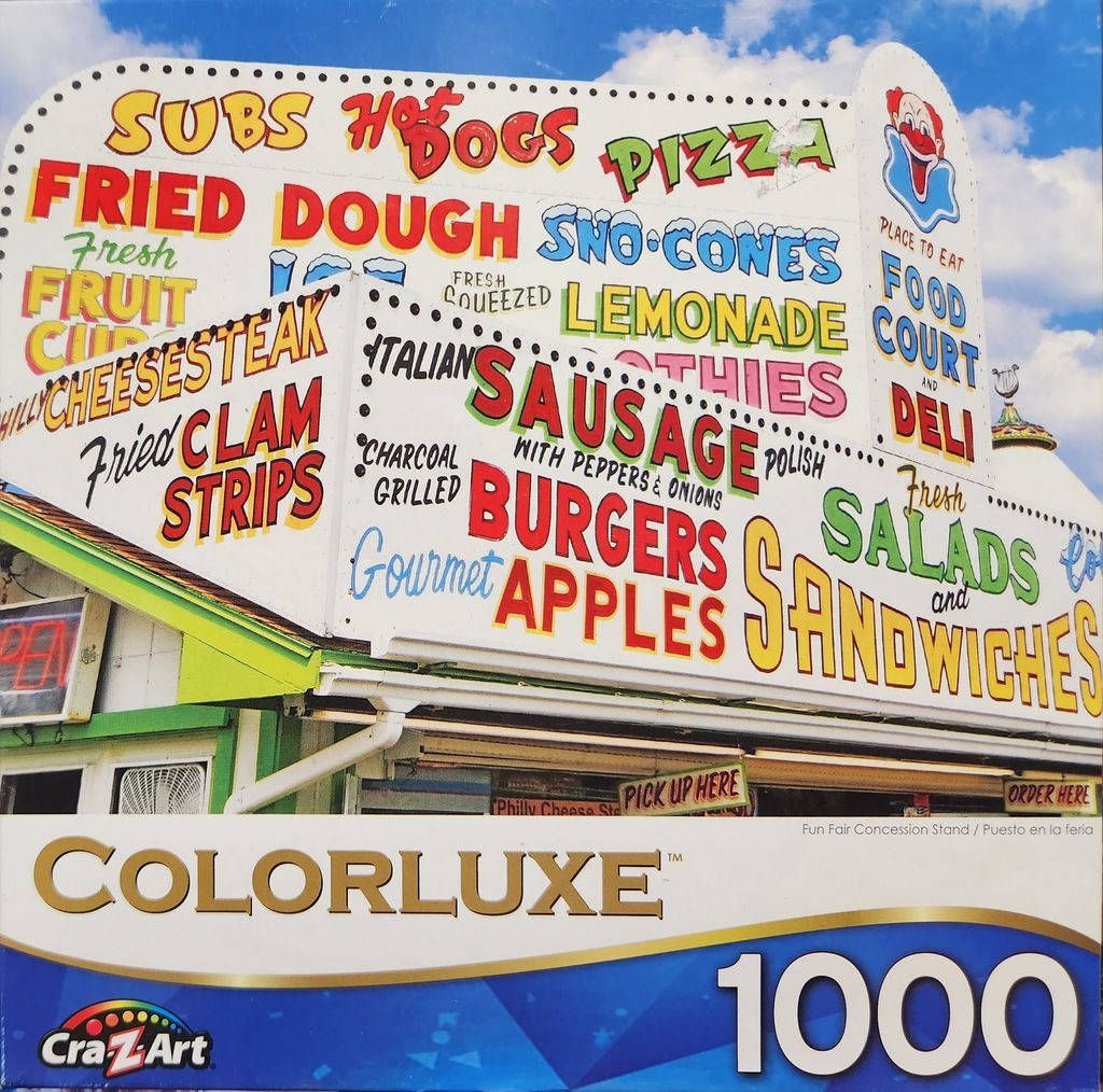 A brightly colored, multi-tiered food stand sign at a fairground against a blue sky.