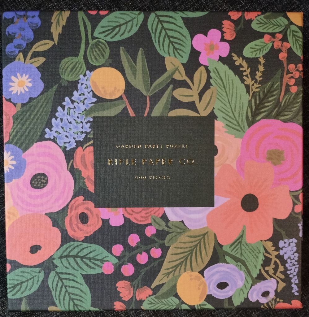 A lush, dark floral pattern featuring pink, coral, and periwinkle blossoms with green foliage.