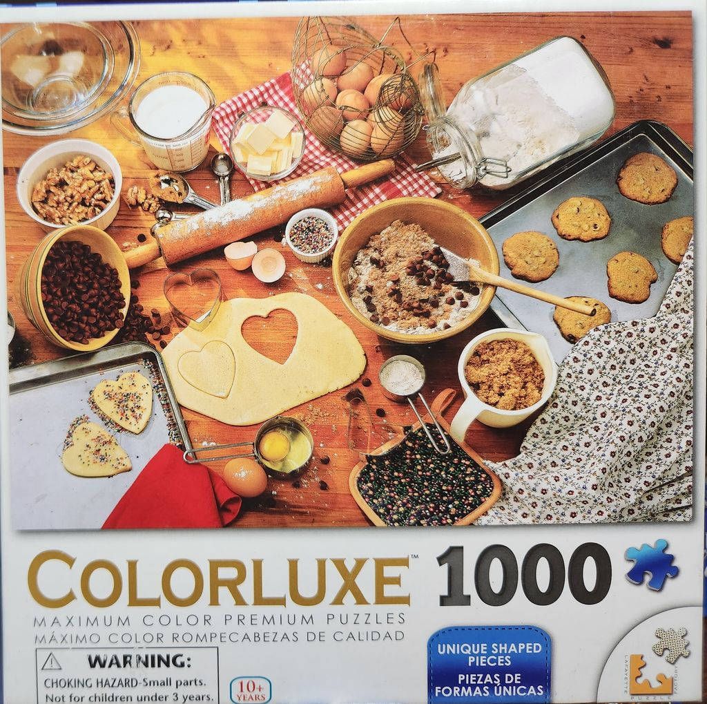 High-angle view of a rustic kitchen counter filled with baking ingredients, bowls of chocolate chips, and heart-shaped cookie
