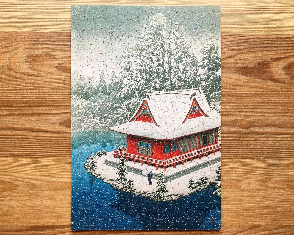 A traditional Japanese red temple building situated on a snowy island surrounded by water in a winter landscape.