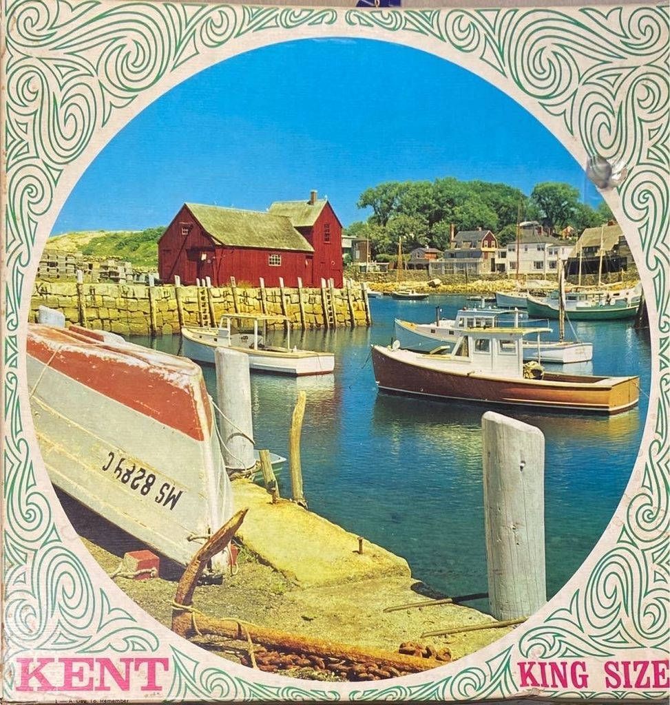 A peaceful coastal harbor scene with a prominent red barn, fishing boats, and a concrete pier.