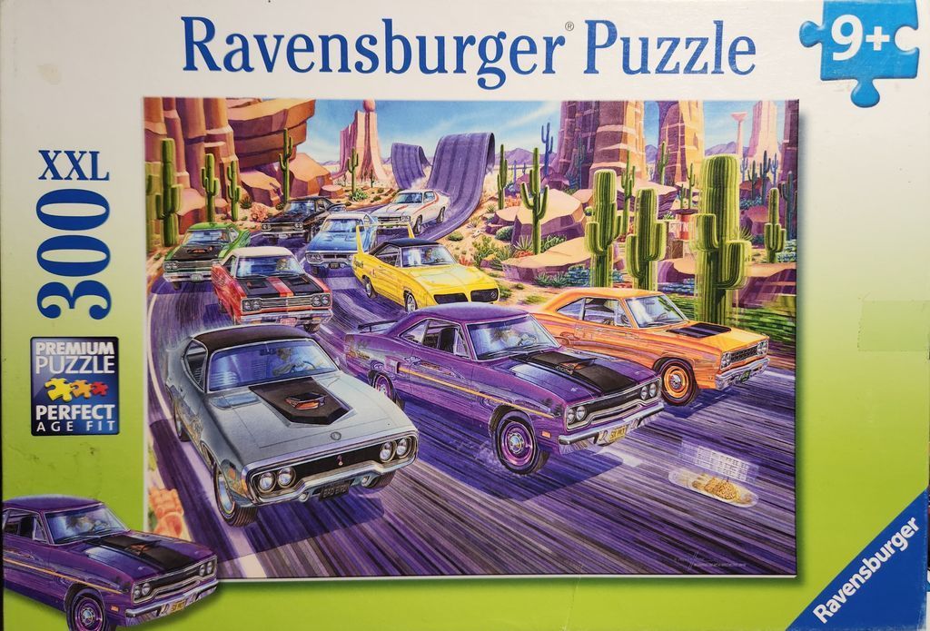 A collection of classic American muscle cars speeding down a desert highway surrounded by cacti and rock formations.