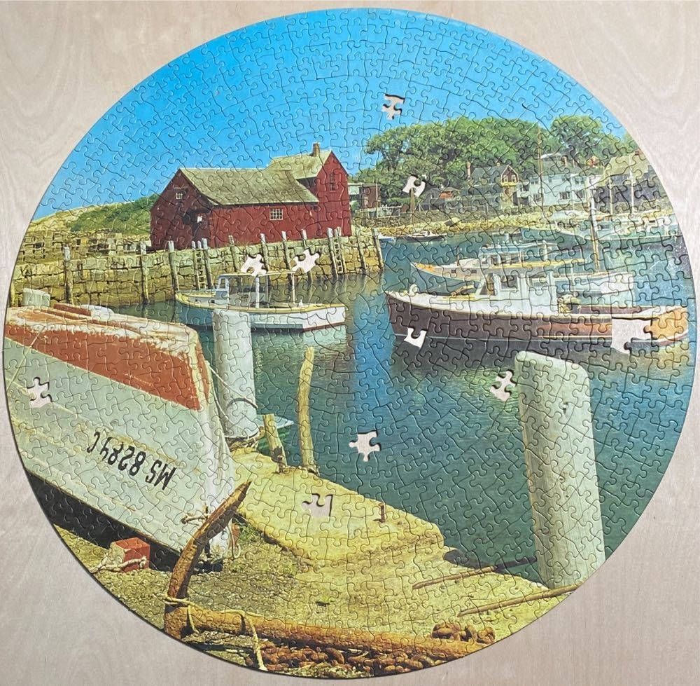 A circular image of a harbor with a red building, docked boats, and a large anchor in the foreground.