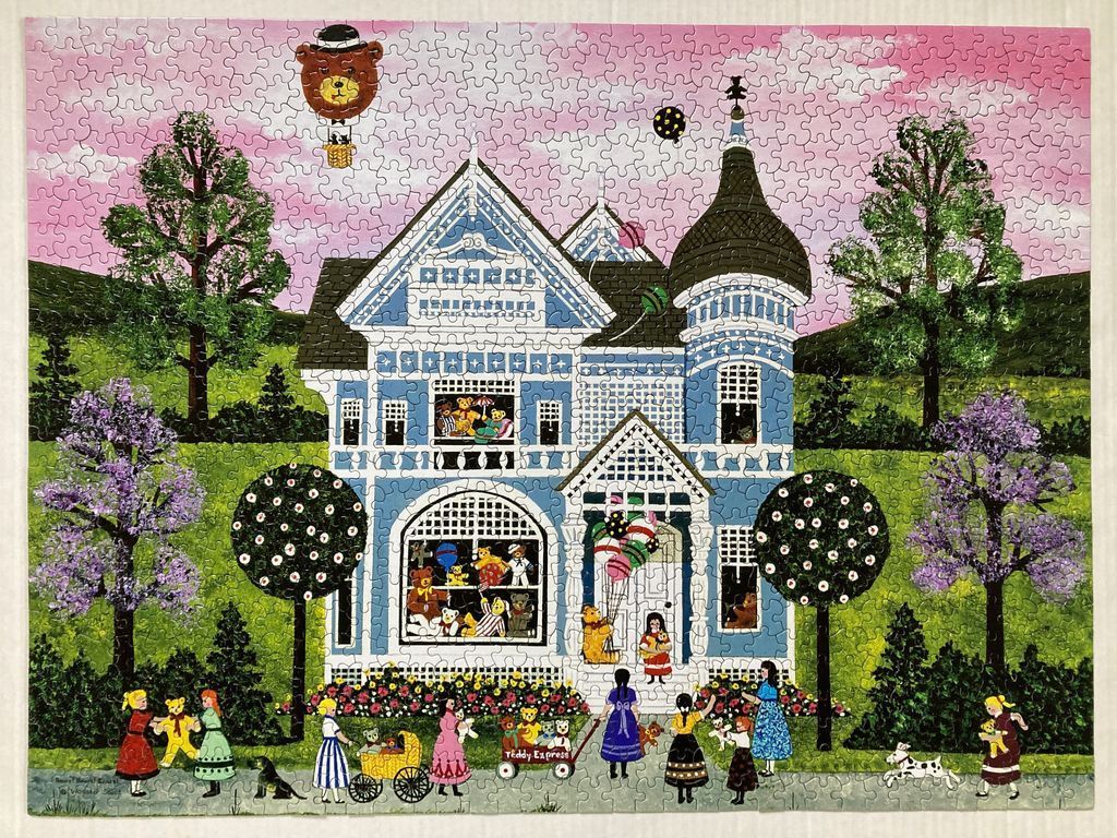 A Victorian house painted blue with teddy bears, children, and a bear-shaped hot air balloon against a pink sky.