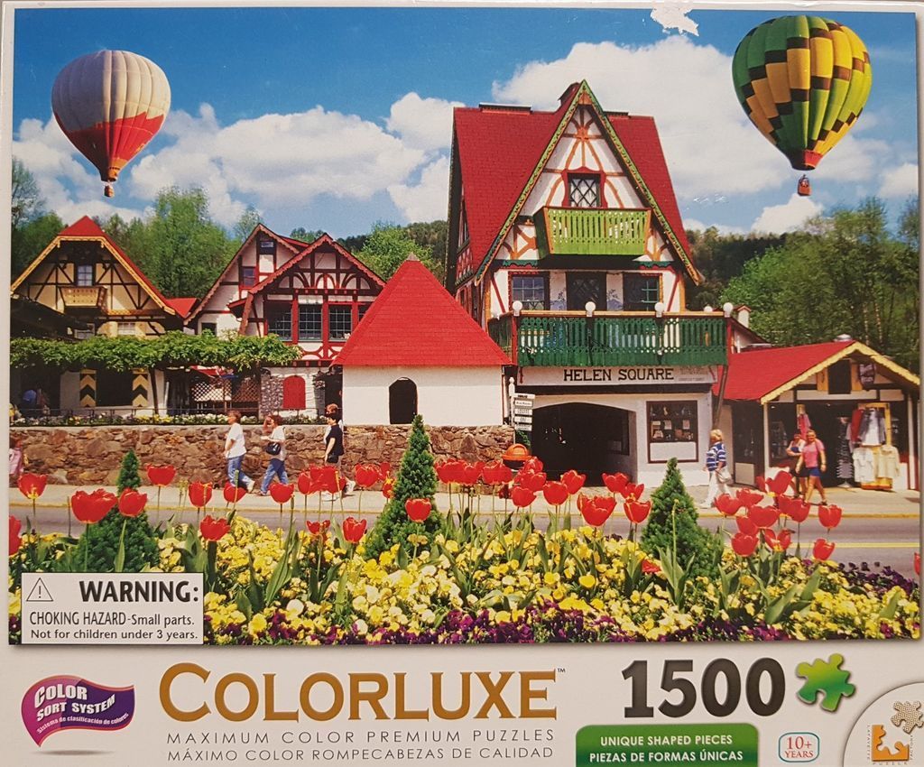 A picturesque European-style village square with red roofs, colorful tulips, and hot air balloons in the sky.