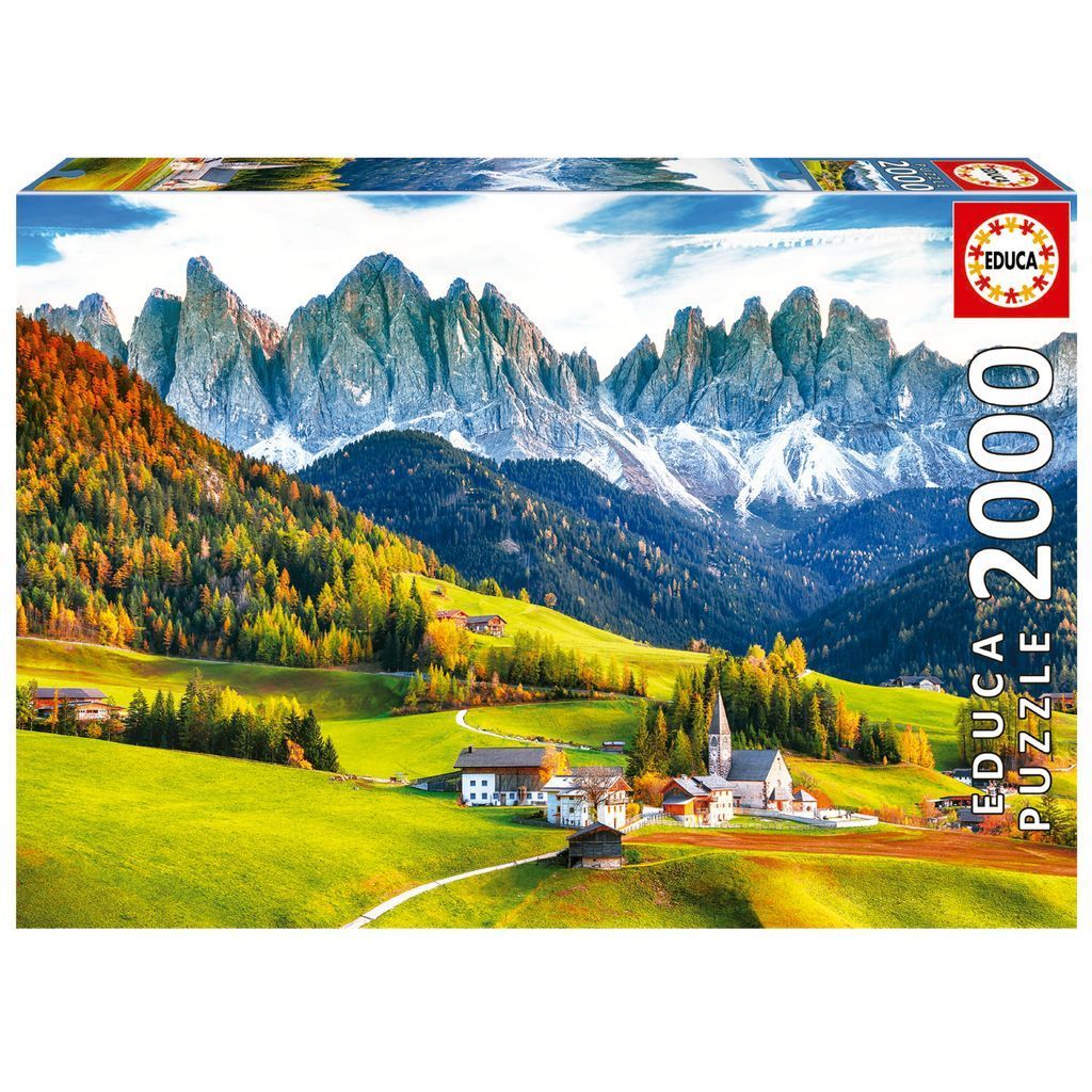 A panoramic landscape featuring the jagged Dolomites mountains rising above a lush, green valley with a small village.