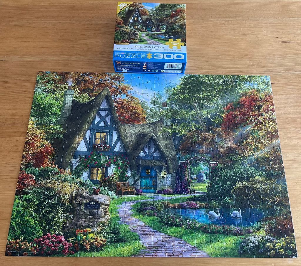 A charming Tudor-style cottage surrounded by vibrant autumn trees and a pond with two white swans.