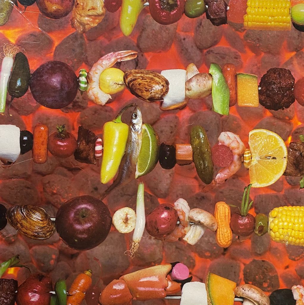 Multiple horizontal skewers of diverse foods suspended over glowing red-hot charcoal embers.