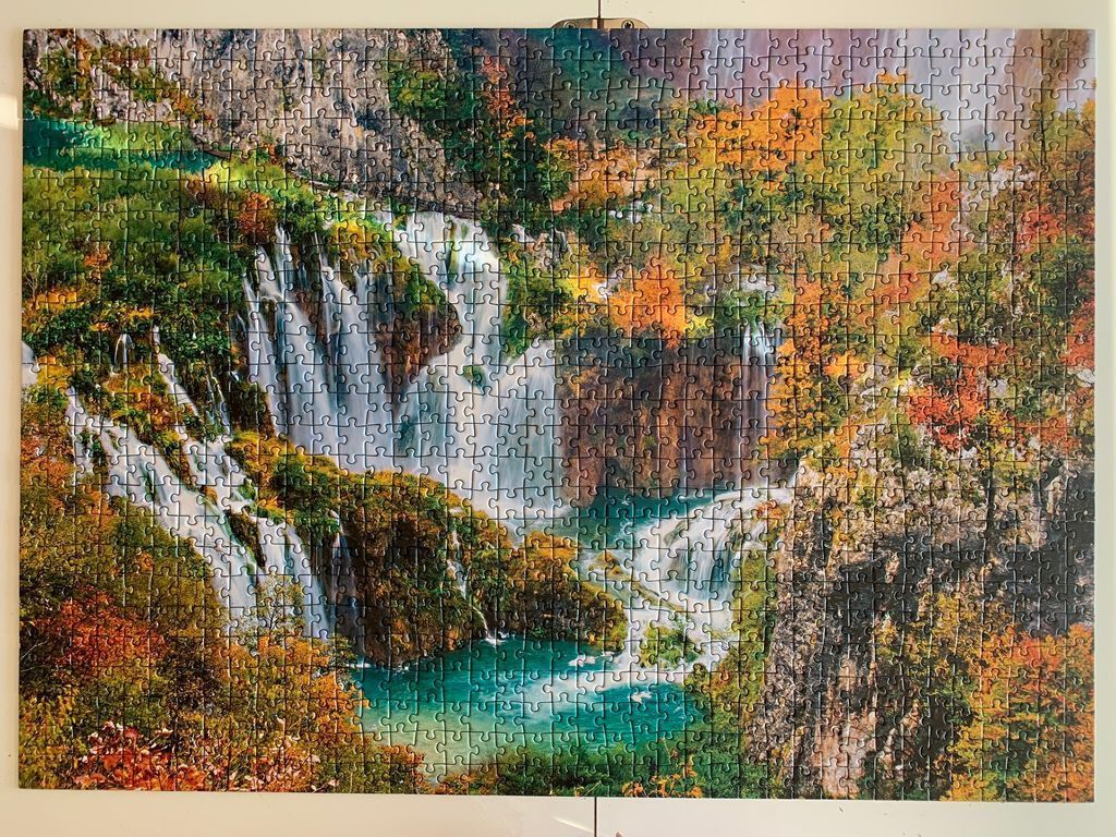 A lush autumn landscape of waterfalls cascading into turquoise pools surrounded by vibrant fall foliage and rocky cliffs.