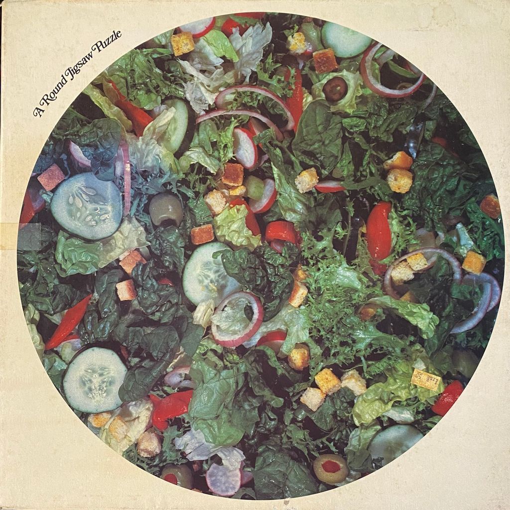 A close-up photograph of a fresh garden salad, presented in a circular format.