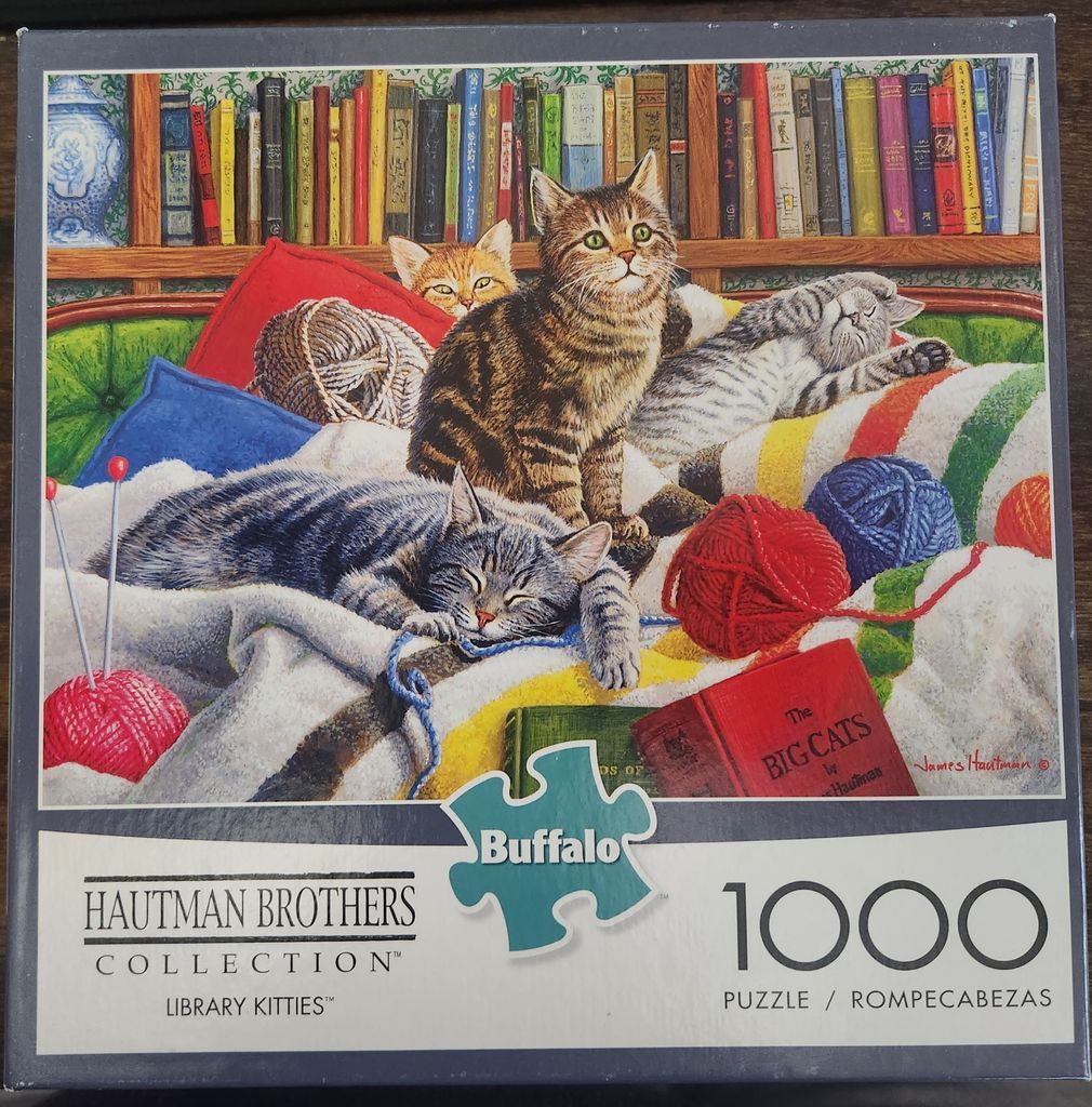 Five cats of various breeds and colours resting among books, knitting yarn, and blankets on a green sofa.