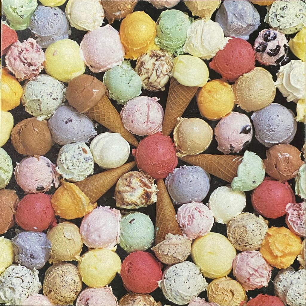 An array of colorful ice cream scoops and several waffle cones against a black background.