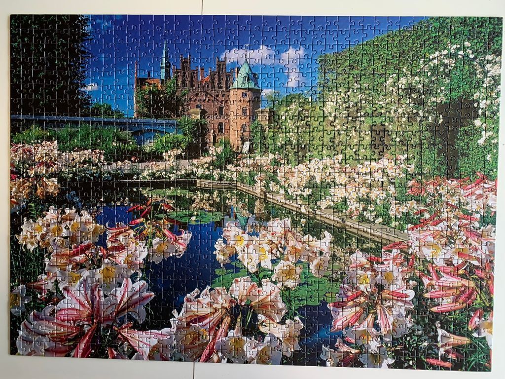 A sunny scene of a brick castle behind a lush garden with a pond and lilies.