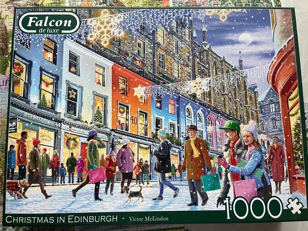 A snowy street scene in Edinburgh at Christmas with people shopping and colorful historic buildings.