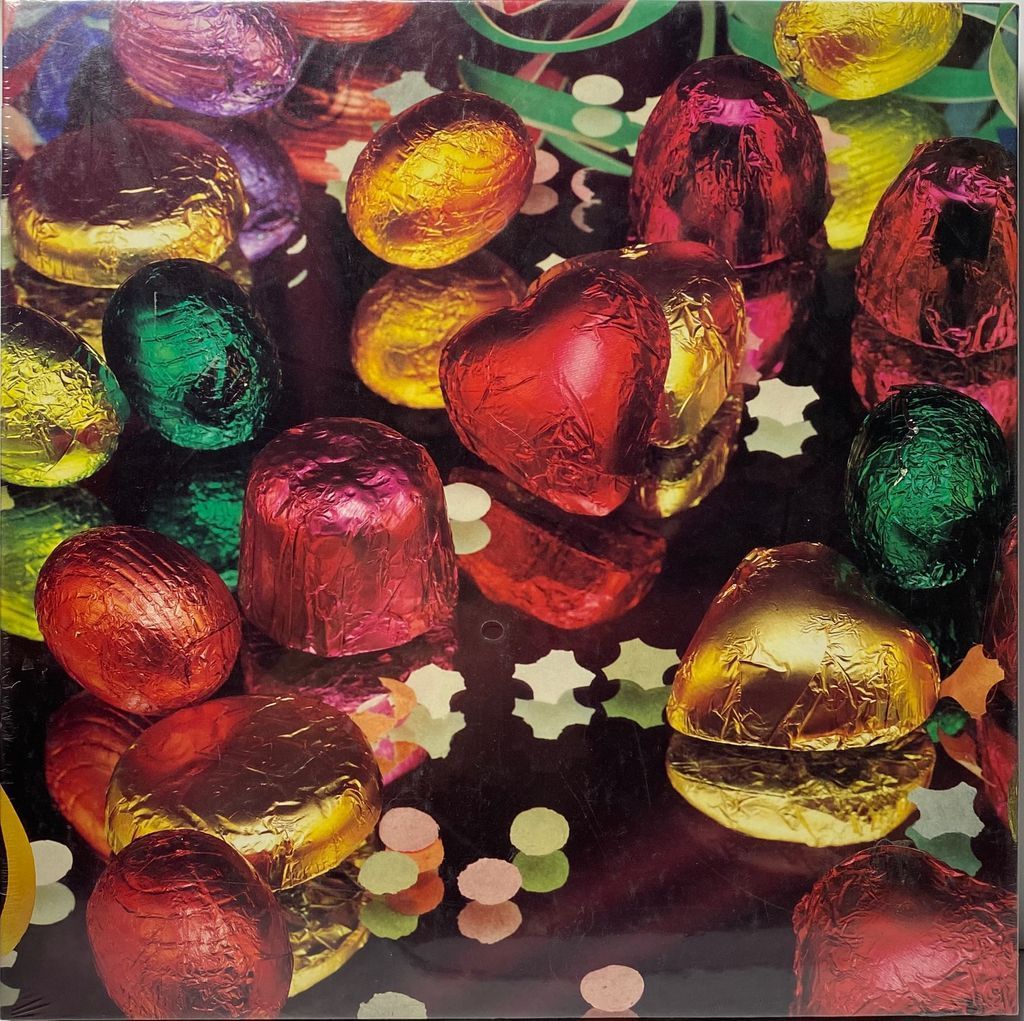 A close-up photograph of assorted chocolate candies wrapped in shiny, colorful foil scattered on a dark, reflective surface.