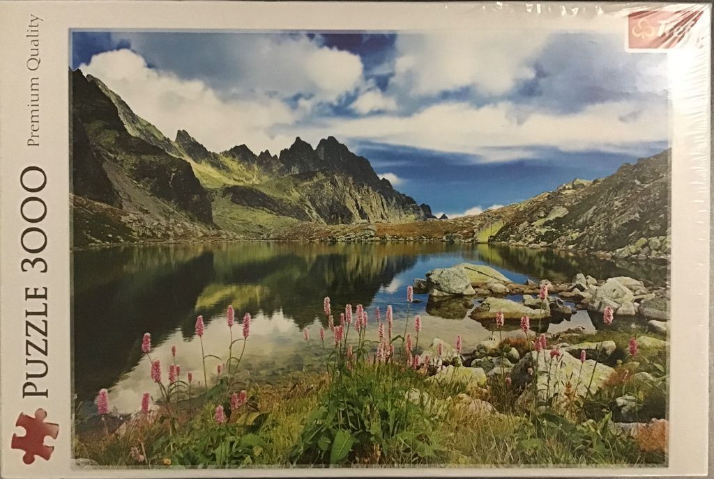 A photograph of a calm mountain lake reflecting sharp, rocky peaks under a sky with scattered white clouds.