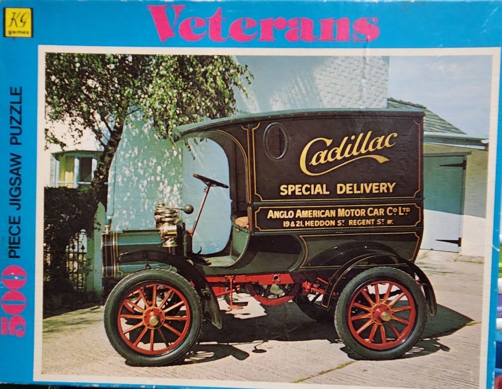 An antique dark green Cadillac delivery truck parked in front of a white building with a tree.