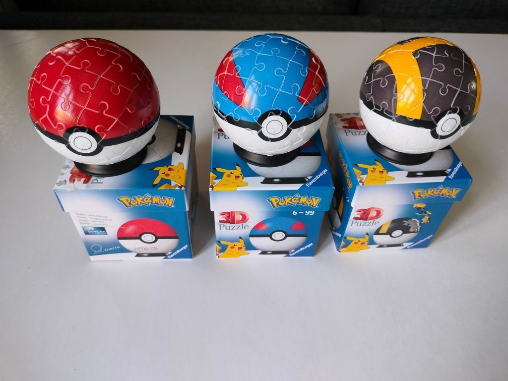 Three spherical Poke Ball toys in red, blue, and yellow sitting on their respective product boxes.