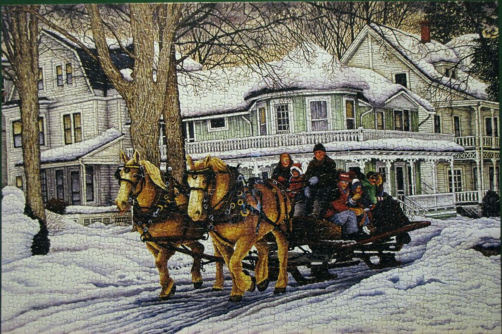 A horse-drawn sleigh carrying a family rides past snow-covered Victorian homes in a winter scene.