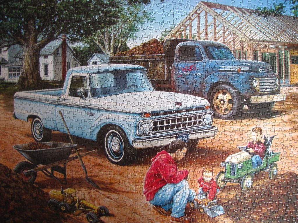 A vintage blue pickup truck and a dump truck at a construction site with a man and children playing.