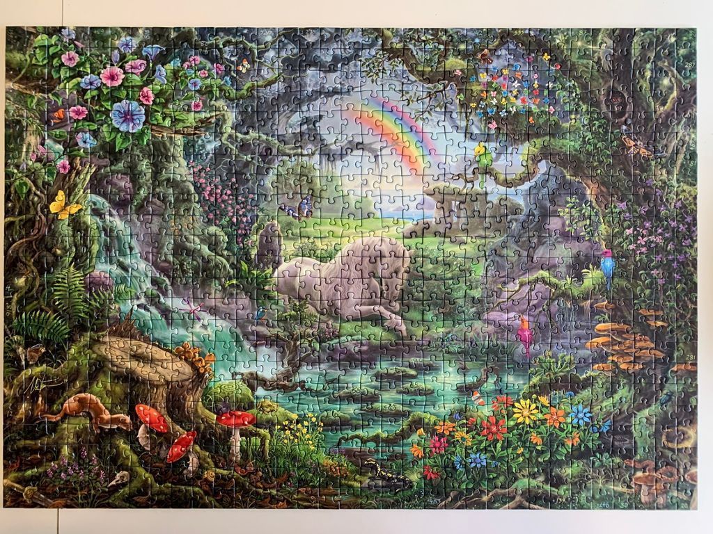Mystical forest scene with a unicorn, rainbow, waterfall, vibrant flowers, and mushrooms.