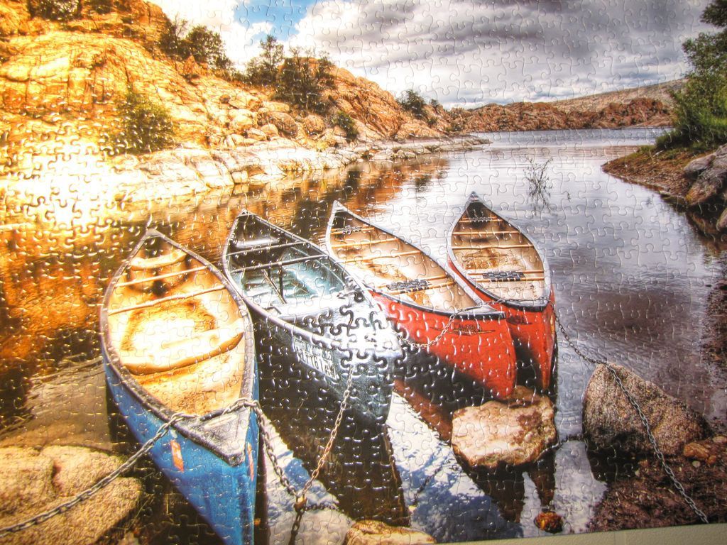 Four canoes moored at the edge of a calm, rocky lake beneath a dramatic sky.