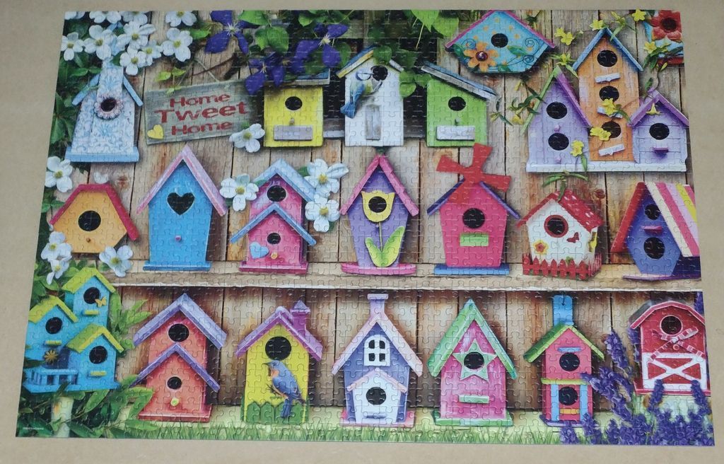 A collection of colorful decorative birdhouses arranged on a wooden fence with floral accents.