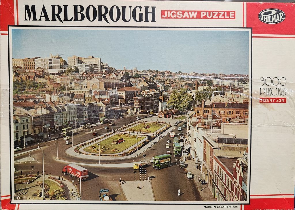 Elevated view of a busy traffic roundabout in a British city featuring historic buildings and a double-decker bus.